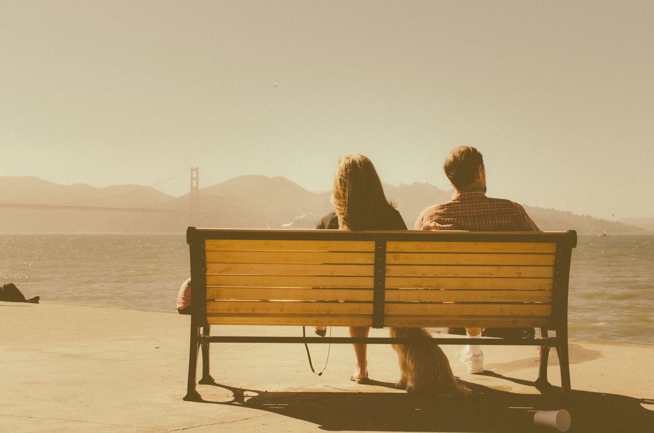A young couple sits on a park bench that overlooks a city skyline.